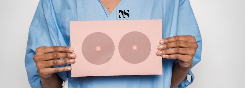 Breast cancer patient in hospital gown holds up an illustration of round breasts in front of her body as she contemplates the truths of breast reconstruction